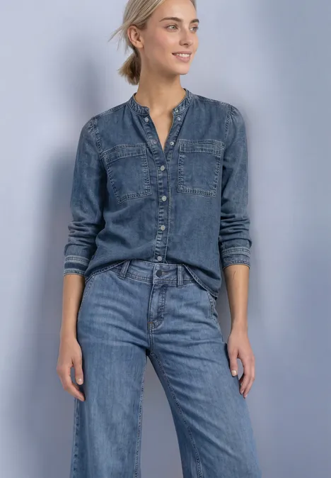 Blouse met lange mouwen en borstzakken Medium Blue Soft washed Jeansbluse und Jeanshose an entspannter Frau vor neutralem Hintergrund