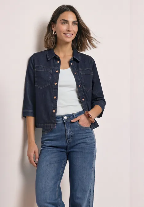 Denim overhemd in rinsed-look Rinse Soft Washed Eine lächelnde Frau in Jeansjacke, weißem Top und blauen Jeans vor hellem Hintergrund.
