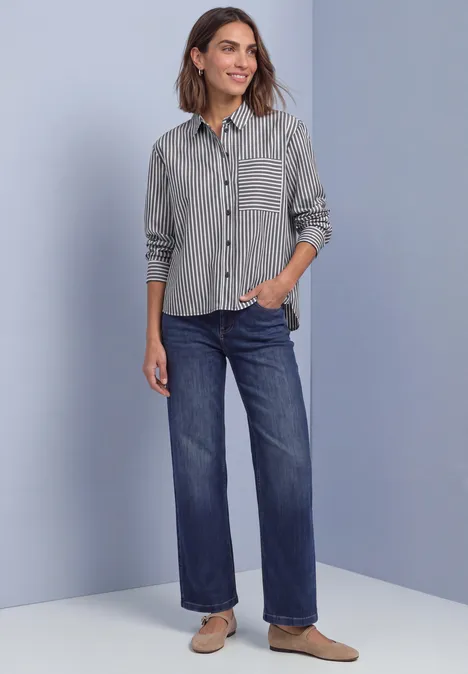 Frau in gestreiftem Hemd, weiten Jeans und flachen Schuhen