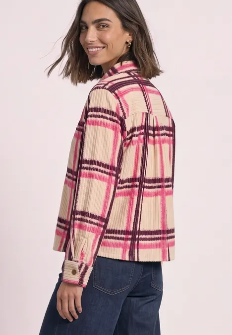 Femme en veste-chemise à carreaux beige et rose et jean, souriante, regard par-dessus l’épaule.