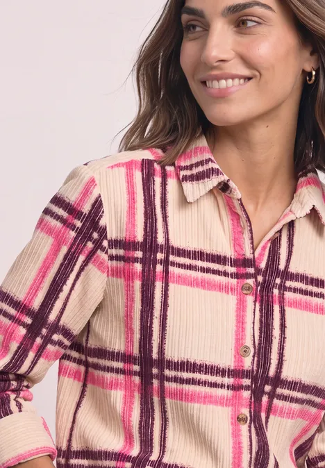 Femme souriante portant une chemise à carreaux beige et rose.