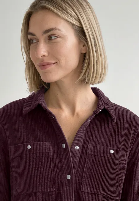Portret van een vrouw met kort blond haar en een wijnrode corduroy blouse, kijkend naar opzij.