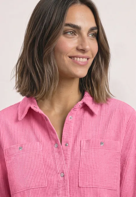 Portret van een glimlachende vrouw met halflang bruin haar en een roze corduroy blouse.
