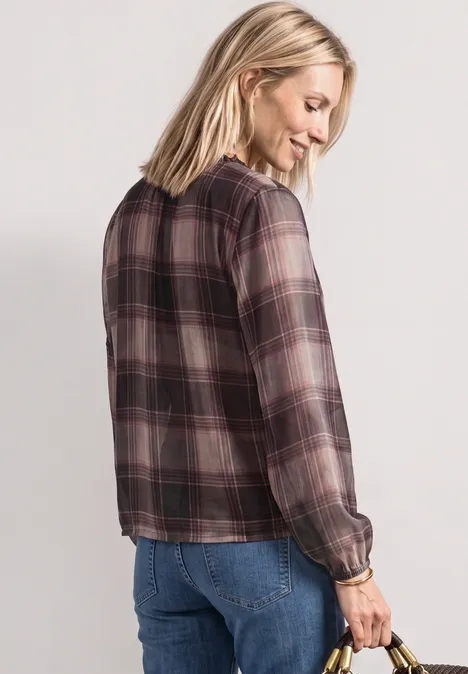 Frau von hinten in kariertem Hemd und Jeans, lächelnd und seitlich schauend.