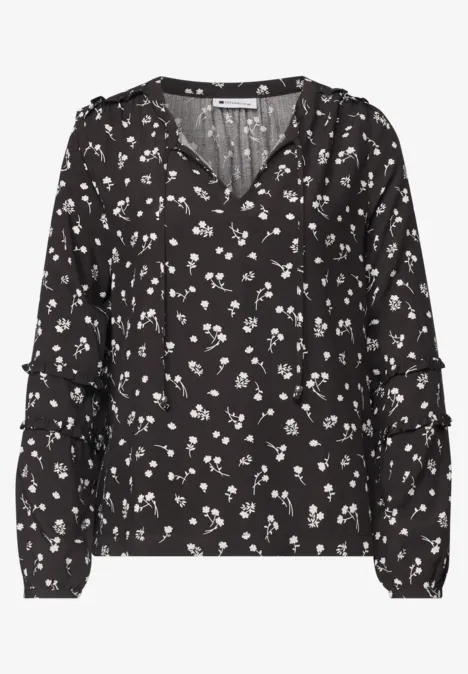 Schwarze Bluse mit weißen Blumenmuster, langen Ärmeln und V-Ausschnitt.