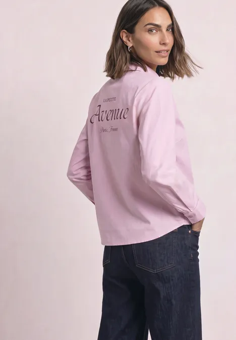 Een vrouw draagt een roze jas met opschrift en een blauwe jeans, kijkt over haar schouder.