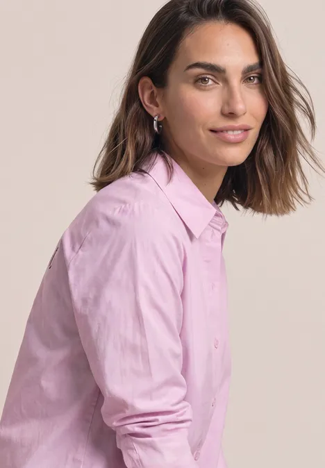Een vrouw in een roze blouse kijkt vriendelijk naar de camera, licht zijwaarts gezeten.