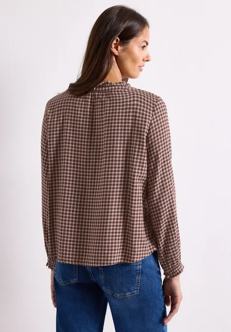 Chemisier à manches longues, col rond et volants warm blush Eine Frau steht mit dem Rücken zur Kamera und trägt eine braun-karierte Bluse.