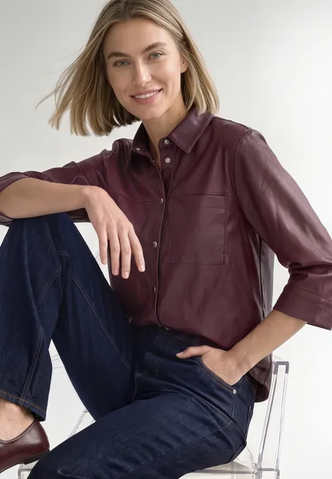 3/4-Arm Hemdbluse im Leder-Look rustic rouge Frau in burgunderfarbener Lederbluse und Jeans sitzt entspannt auf durchsichtigem Hocker und lächelt.