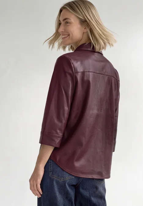 3/4-Arm Hemdbluse im Leder-Look rustic rouge Frau trägt burgunderrotes Lederhemd und Jeans, schaut über die Schulter und lächelt leicht.