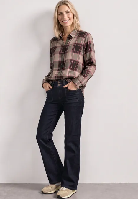 Langarm Hemdbluse mit Karomuster sanded amber Frau mit kariertem Hemd und dunklen Jeans lächelt entspannt, Hände in den Taschen.