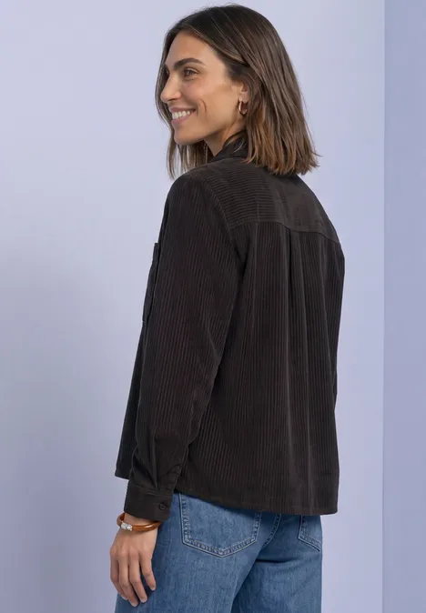 Femme souriante de profil portant une veste en velours côtelé marron et un jean bleu sur fond pastel