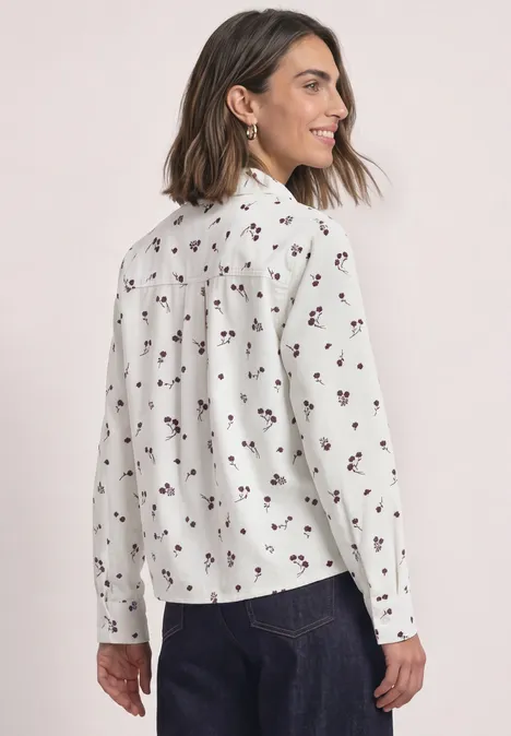 Frau von hinten in weißer Bluse mit kleinem Blumenmuster und dunkler Hose.