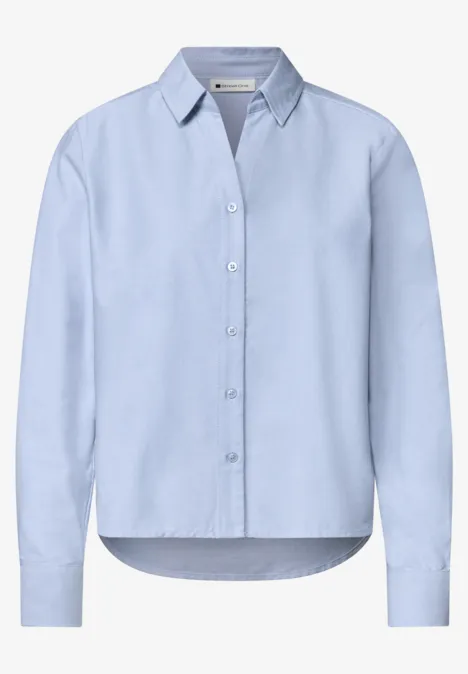 Chemisier bleu clair manches longues, col classique et patte de boutonnage, coupe légèrement cintrée.