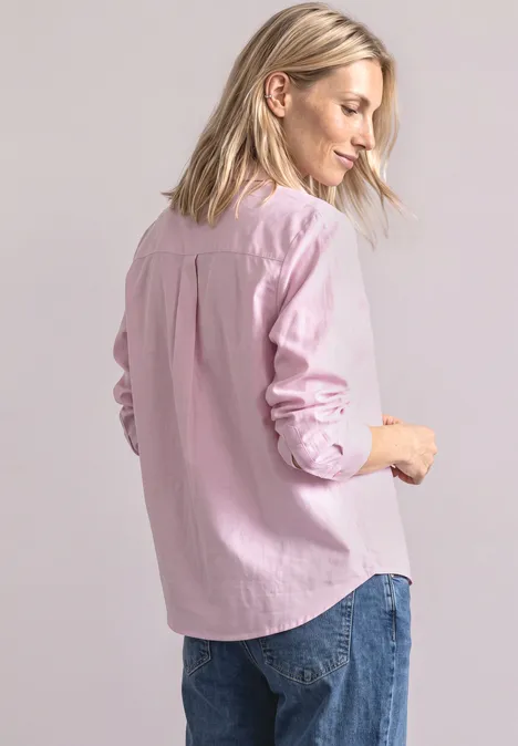 Une femme vue de dos portant une chemise rose et un jean, sur fond clair.