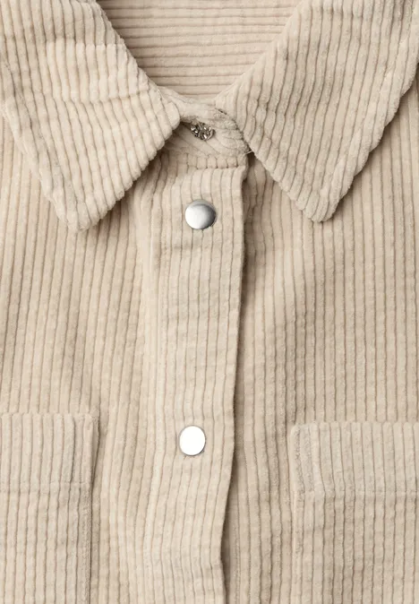 Nahaufnahme des Frontteils einer beigen Cord-Hemdjacke mit silbernen Druckknöpfen und aufgesetzten Taschen.