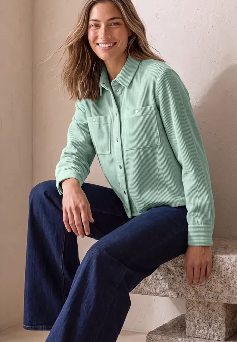 Eine lächelnde Frau sitzt auf einem Steinblock, trägt ein mintgrünes Hemd und dunkle Jeans.