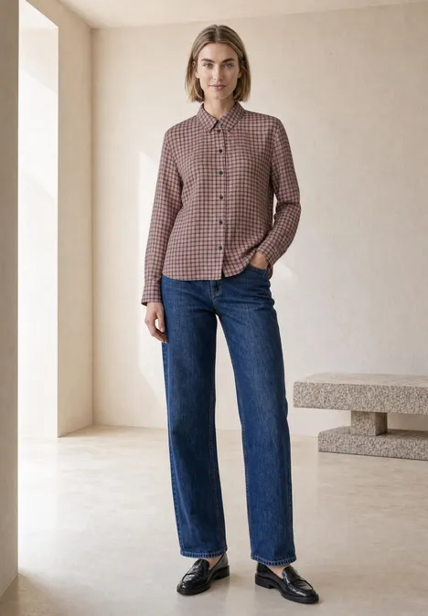 Langarm Hemdbluse mit Karomuster warm blush Eine Frau steht in minimalistischem Raum, trägt karierte Bluse, gerade geschnittene Jeans und schwarze Loafers.