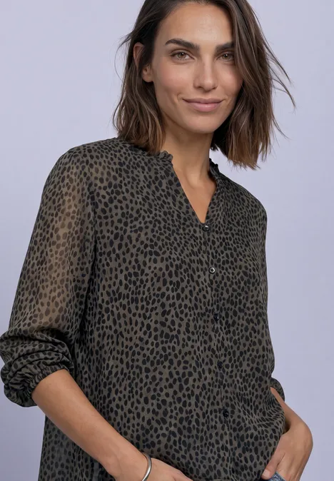 Femme aux cheveux mi-longs bruns portant un chemisier ample à imprimé léopard, main dans la poche.