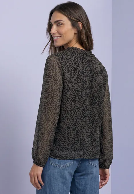 Femme vue de dos, regard par-dessus l'épaule, chemisier chiffon noir à pois beiges et jean sur fond clair.