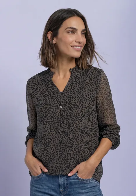 Femme souriante portant une blouse à motifs foncés, col en V et manches retroussées, devant un fond clair