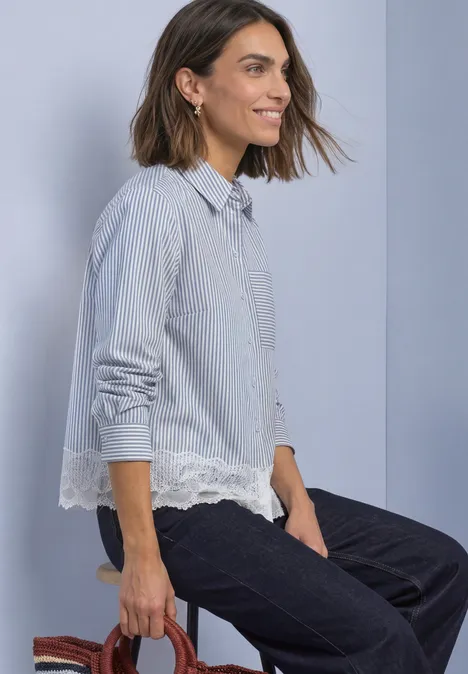 Overhemd met lange mouwen, strepen en kanten rand northern blue Frau mit halblangem Haar in blau-weiß gestreiftem Hemd mit Spitze sitzt seitlich auf einem Hocker.