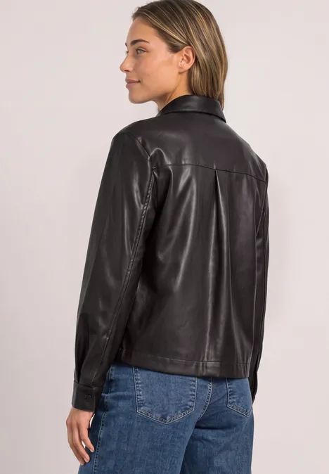 Frau von hinten in schwarzer Lederbluse und Jeans, seitlich blickend.