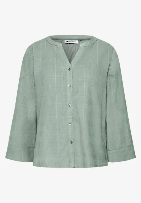 Blouse ample vert pastel, col en V, patte de boutonnage et manches larges.