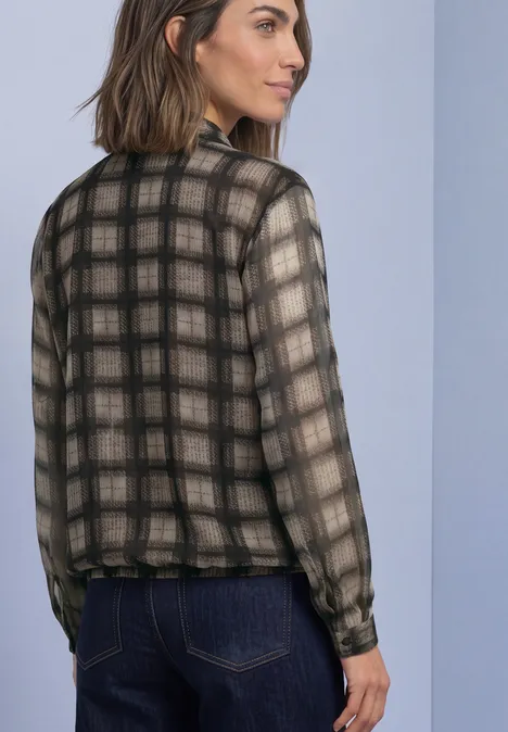 Chiffonblouse met strikdetail sanded amber Vrouw draagt halftransparant geruit langarmshirt in zwart-beige, staand opzij met een blik over haar schouder.