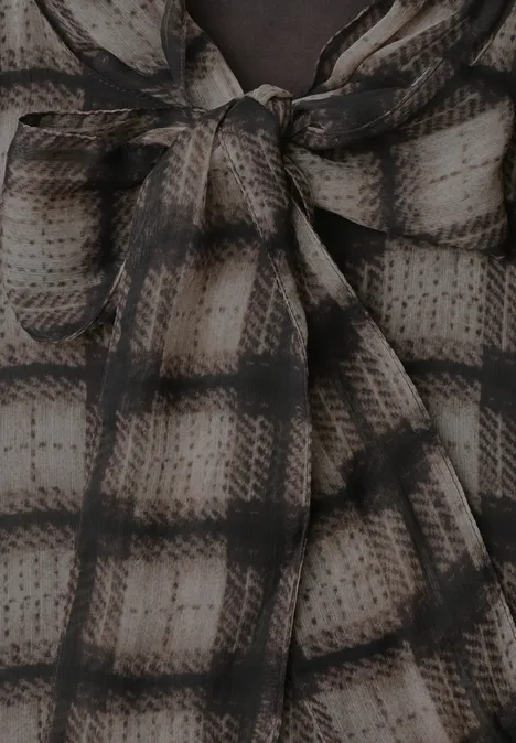 Chiffonblouse met strikdetail sanded amber Close-up van een crème-zwart geruit stof die in een strik bij de halslijn is gebonden.