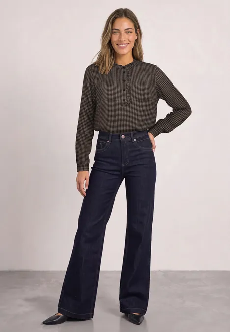 Frau in hochgeschnittener Flared-Jeans und schwarzem Langarm-Oberteil vor hellem Hintergrund.