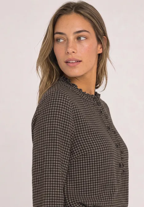 Junge Frau im karierten, rüschenbesetzten Blusenshirt blickt seitlich, lässig und elegant.