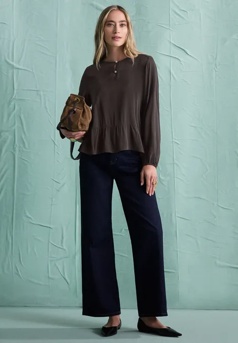 Chemisier à manches longues et à basque black coffee Une femme portant un haut marron à manches longues, un pantalon bleu foncé large et des escarpins noirs, avec un sac marron.