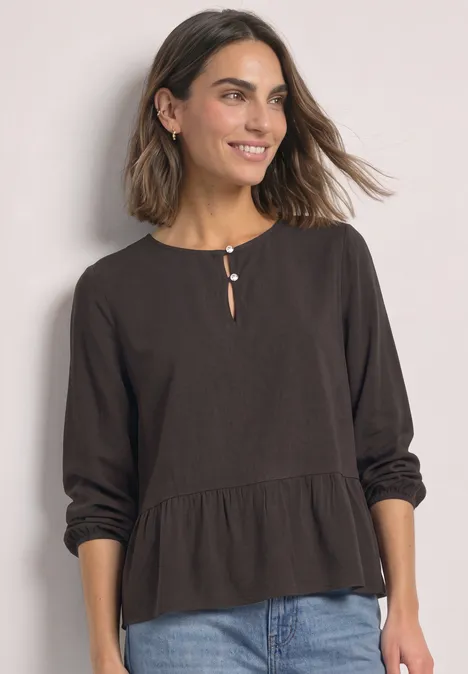 Chemisier à manches longues et à basque black coffee Femme porte un chemisier noir ample à manches longues, détail bouton à l’encolure et coupe décontractée avec un jean.