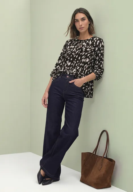 Chemisier à manches longues avec volant et imprimé cerf Black Une femme porte un chemisier noir et blanc, un pantalon bleu marine et un sac marron.