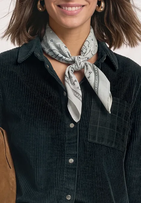 Frau in schwarzer Cord-Hemdjacke mit grauem Halstuch und goldenen Creolen lächelt.