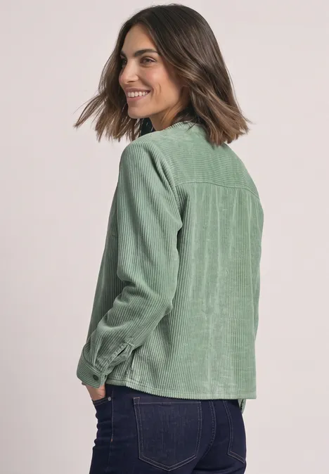 Frau von hinten in grüner Cordjacke mit langärmligem Hemd, schaut lächelnd zurück.