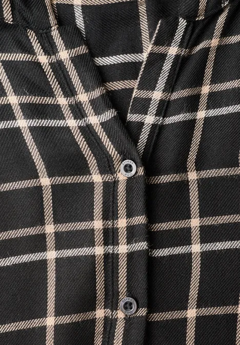 Nahaufnahme eines schwarz-beige karierten Kleidungsstücks mit zwei Knöpfen.
