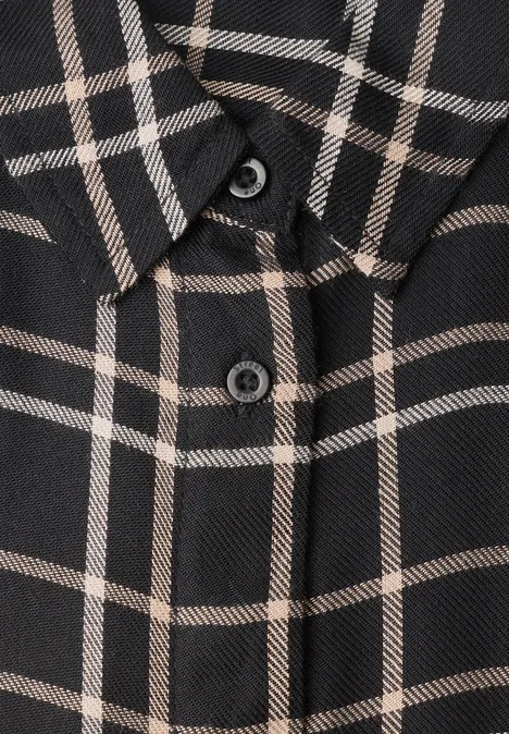 Gros plan d’une chemise sombre à carreaux beiges avec boutons visibles.