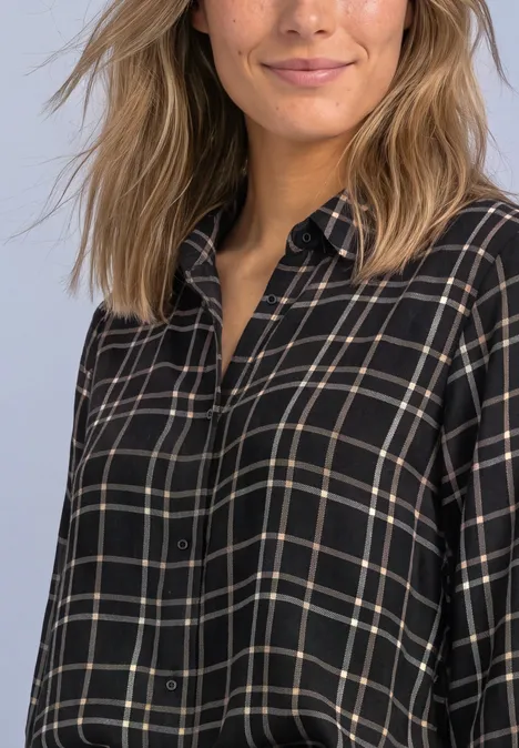 Femme avec chemise noire à carreaux, souriant légèrement.