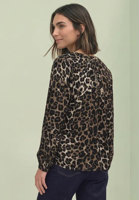 Eine Frau in leo gemustertem Langarmshirt und Jeans blickt über die Schulter.