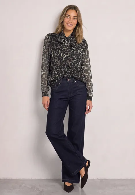 Langarm Chiffon-Bluse mit Schleifendetail Black Frau trägt dunkle Schlagjeans und Animal-Print-Bluse, steht lächelnd vor hellem Hintergrund.