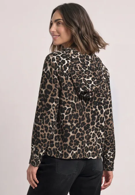 Frau im Leoparden-Kapuzenshirt, langärmelig, blickt über die Schulter, kombiniert mit schwarzer Hose.