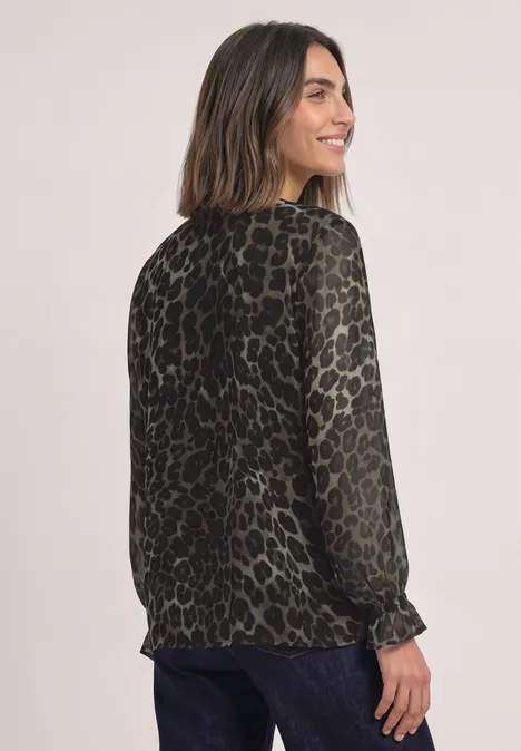 Frau trägt grüne, semi-transparente Bluse mit Animal-Print, schaut lächelnd über die Schulter.