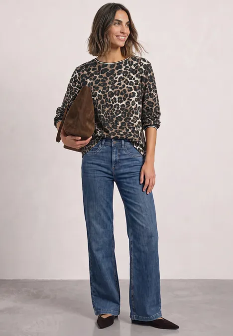 Frau trägt lässiges Leopardenmuster-Oberteil, blaue Jeans mit weitem Bein und braune Handtasche.