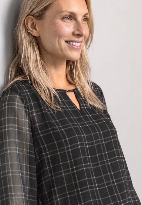 Eine blonde Frau lächelt und trägt eine schwarze, karierte Bluse.