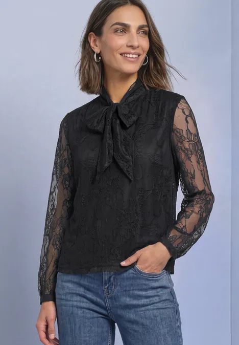Langarm Bluse aus Spitze mit Schleifendetail Black Frau trägt schwarze Spitzenbluse mit Schleife und blauen Jeans.