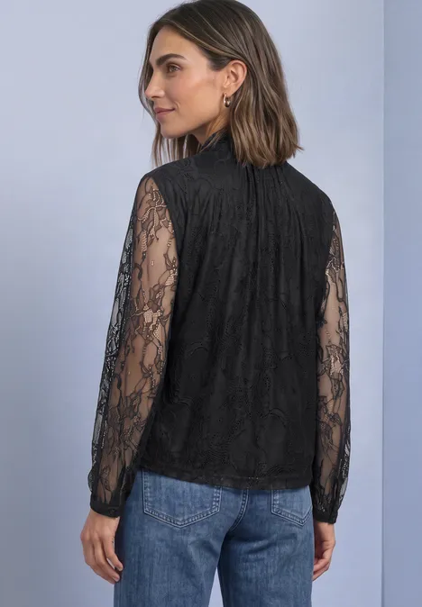 Langarm Bluse aus Spitze mit Schleifendetail Black Frau von hinten in schwarzer Spitzenbluse mit langen Ärmeln und blauen Jeans vor neutralem Hintergrund.