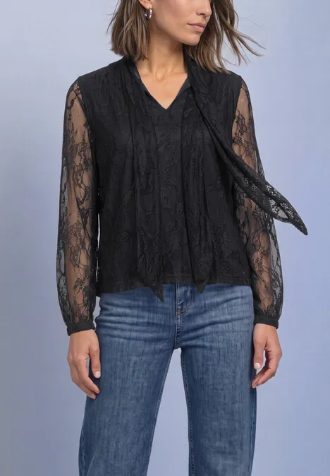 Langarm Bluse aus Spitze mit Schleifendetail Black Frau trägt schwarze Spitzenbluse mit langen Ärmeln und blauen Jeans vor neutralem Hintergrund.
