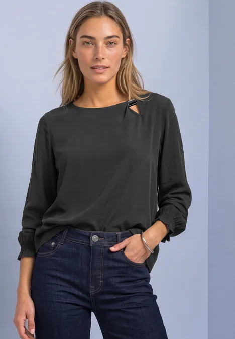 Blouse met ronde hals en gespdetail armor grey Vrouw in zwarte blouse met uitsnede bij de kraag, donkerblauwe jeans, ontspannen pose voor neutrale achtergrond.